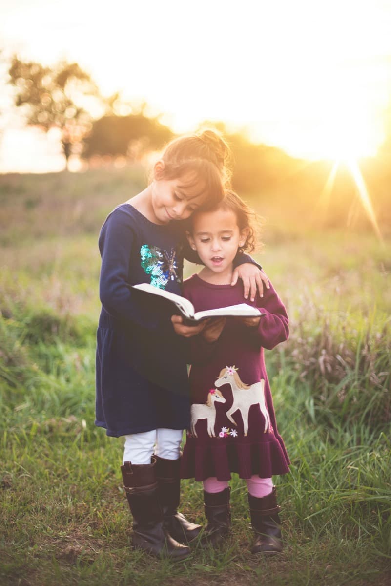 Zwei Mädchen lesen gemeinsam ein Buch – Kosten einer Kinderzusatzversicherung in Österreich im Vergleich
